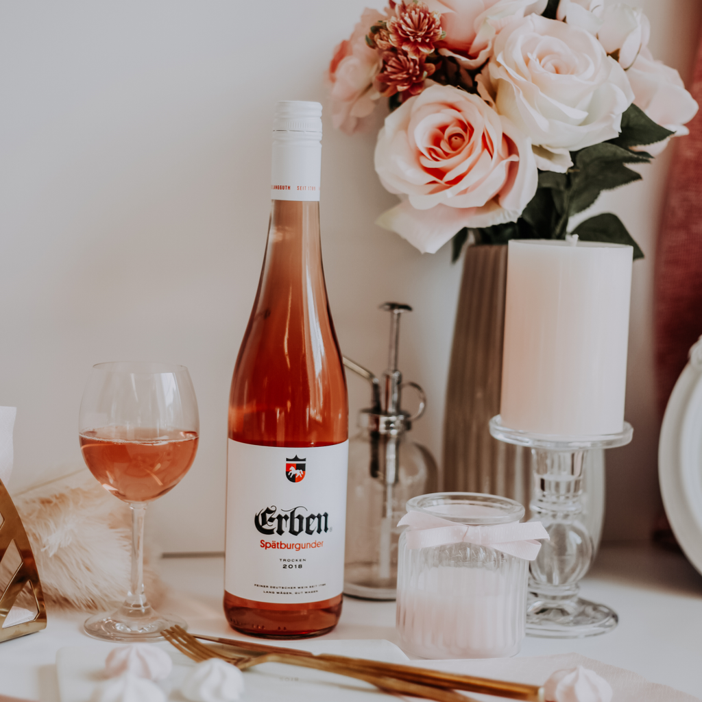 ERBEN Spätburgunder Rosé Trocken 0,75l - Roséwein - stehend auf einem Tisch mit weißen Kerzen und hellrosa Rosen